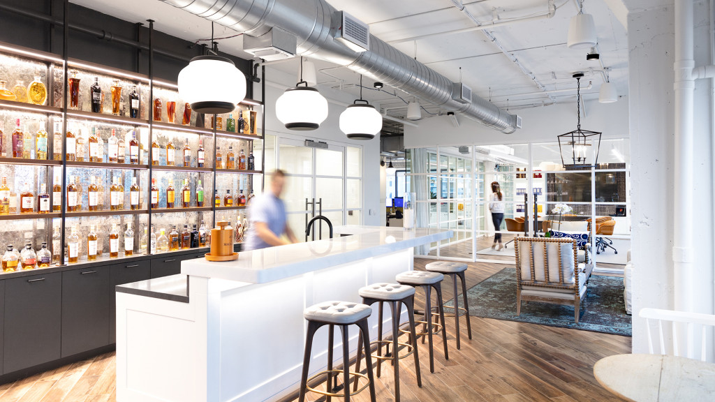A bar with stools and a counter with bottles of alcohol.